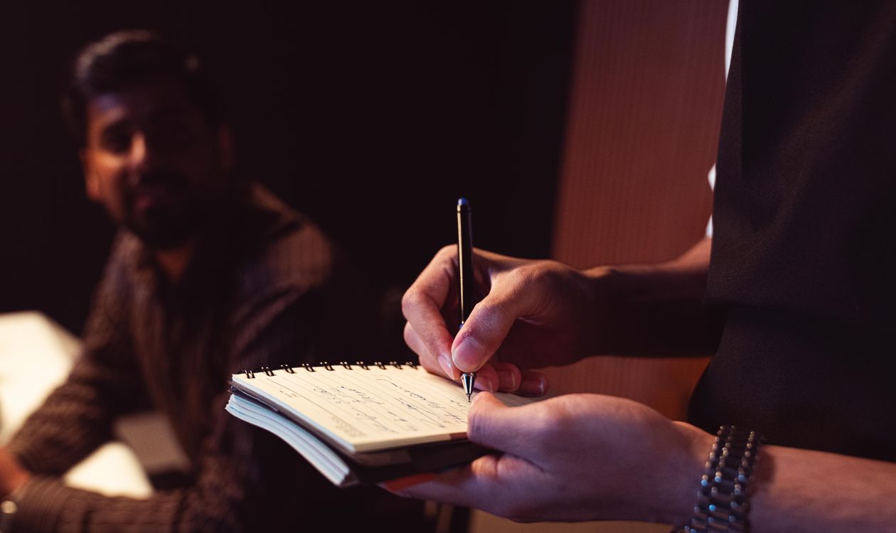 Close-up of hands writing carefully in a notebook during a conversation, representing the Solution-Focused discipline of attending to the client's exact words